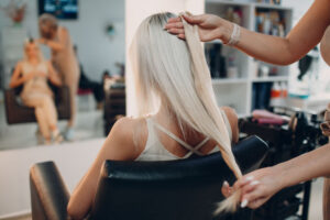 Hairdresser female making hair extensions to young woman with blonde hair in beauty salon. Professional hair extension salon