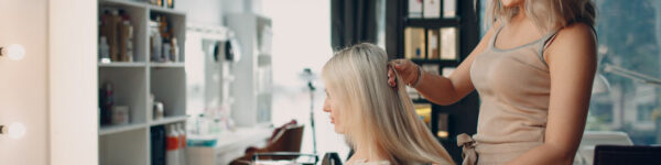 Hairdresser female making hair extensions to young woman with blonde hair in beauty salon. Professional hair extension